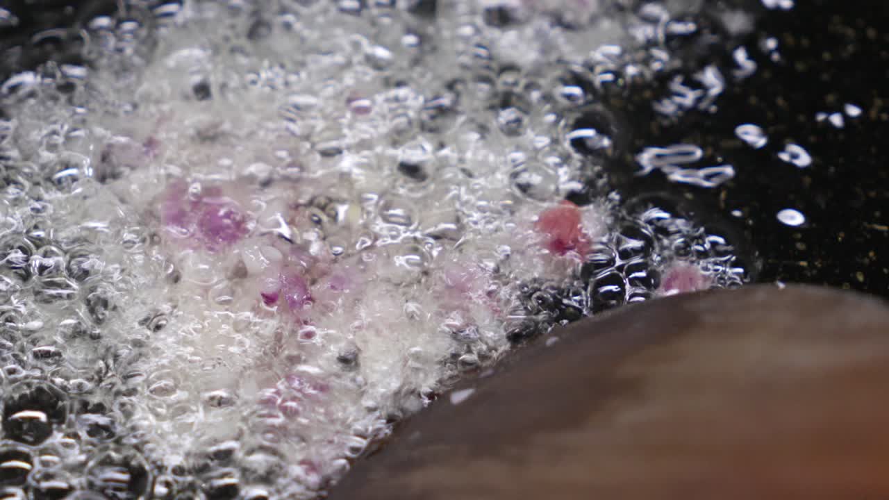 Primo piano di cipolla rossa che frigge e sfrigola in una padella calda con olio, diventando lucida e morbida per la base di una ricetta, perfetta per cucinare, la preparazione dei pasti e i contenuti alimentari.