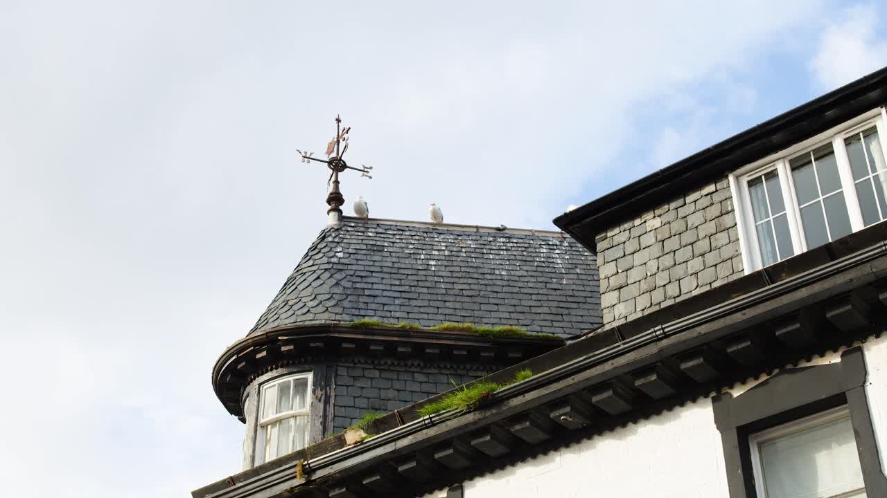 Camera slowly pans across historic slate roof with weather vane, soft daylight, minimal movement