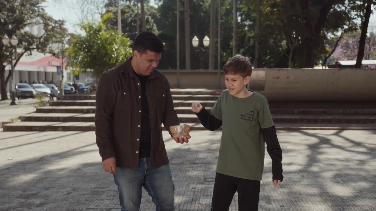 A man and a boy interacting in a park, sharing food and observing their surroundings