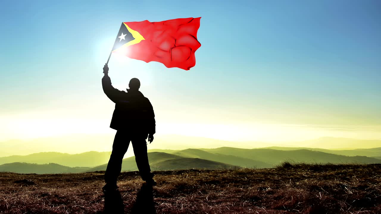 hombre ganador de silueta exitosa agitando la bandera de timor oriental en la cima del pico de la montaña. fondo de bucle de cinemagraph