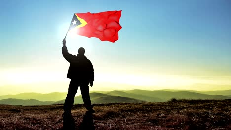 hombre ganador de silueta exitosa agitando la bandera de timor oriental en la cima del pico de la montaña. fondo de bucle de cinemagraph