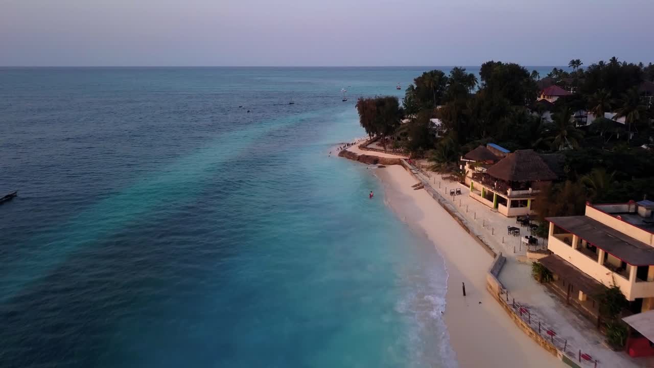 Spectacular Drone Aerial Pullback over Amazing Blue Green Ocean Waters with Beach Front Luxury Hotels and Properties Zanzibar, Unguja, Island in Tanzania During Sunset