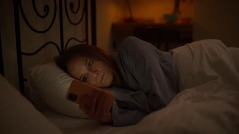 woman using phone in bed at night