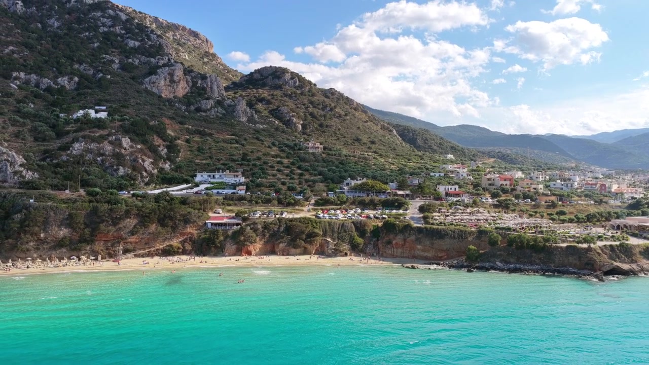 Vista aérea de drone de uma praia de areia turquesa vívida e bar de praia abaixo de uma montanha íngreme, Praia de Voulisma, Grécia