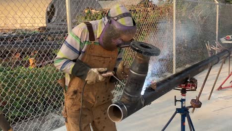 static shot of a welder working on a large piece of metal pipe himself