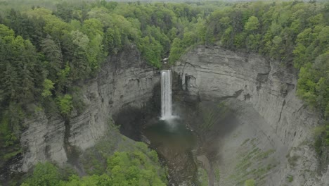 drone shot, flying to the right, showing a big waterfall, in a canyon with trees surrounding it