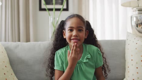 Happy-biracial-girl-sitting-on-sofa-using-sign-language