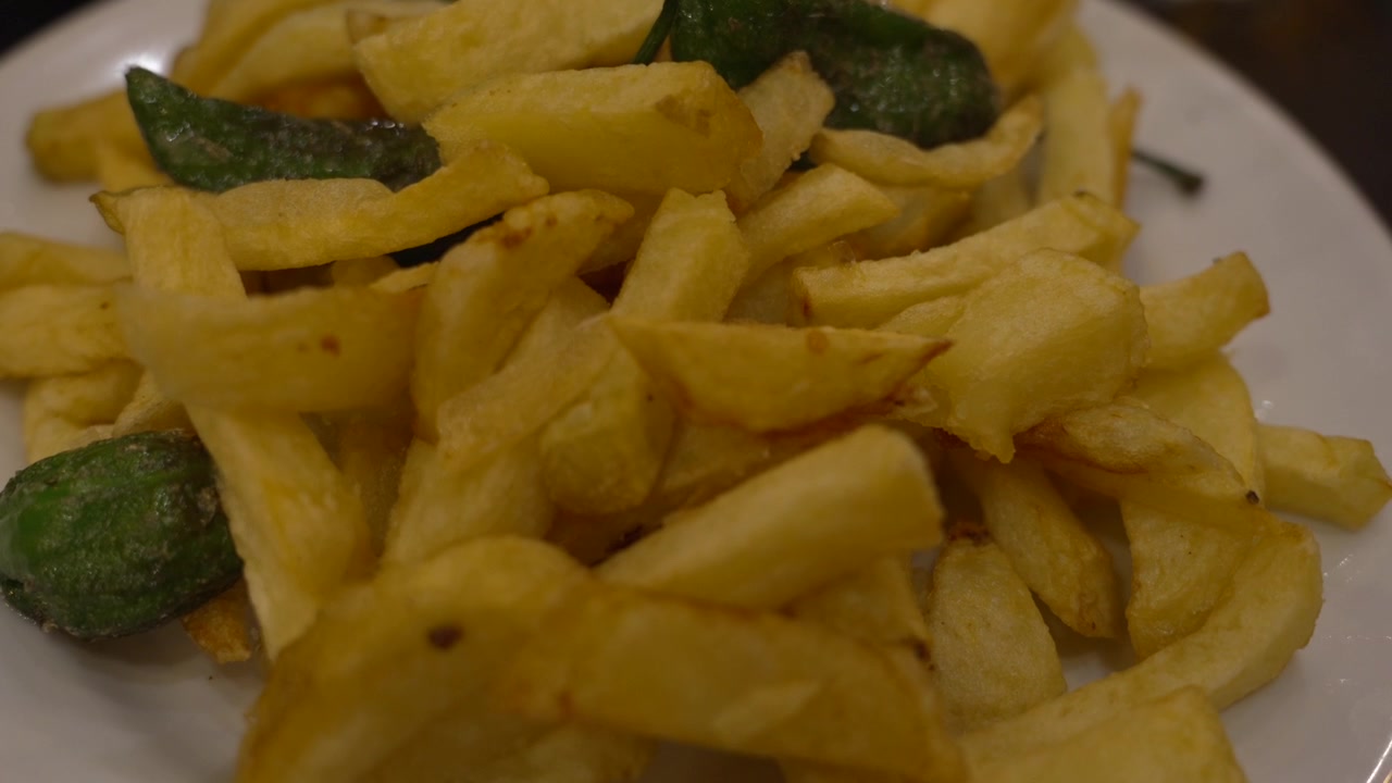 Golden fried potato chips and vibrant green Padron peppers creating a classic Spanish tapa, offering a delicious appetizer from Mediterranean cuisine