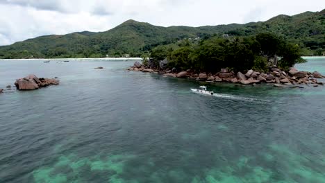 Vista-Aérea-De-Un-Barco-Blanco-Flotando-Junto-A-Una-Isla-Rocosa-Frente-A-La-Costa-De-Praslin,-Las-Seychelles