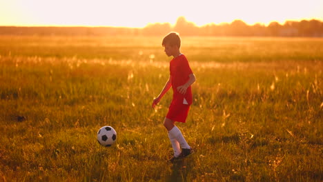 Boy-Junior-in-a-red-t-shirt-and-sneakers-at-sunset-juggling-a-soccer-ball-training-and-preparing-to-become-a-football-player.-The-path-to-the-dream.-Hard-work