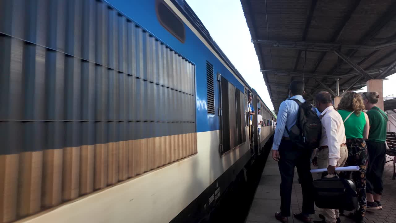 A train approaches the platform at Kandy Station surrounded by lush greenery in Sri Lanka. Passengers wait eagerly, capturing a sense of travel and anticipation.