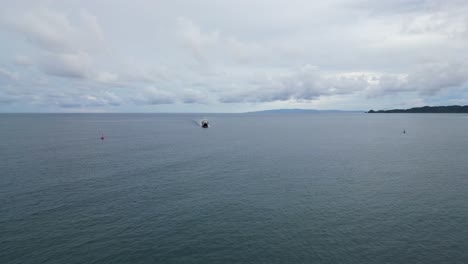An-aerial-shot-of-a-ferry-sailing-towards-a-vast-ocean,-with-an-island-and-cloudy-sky-in-the-background