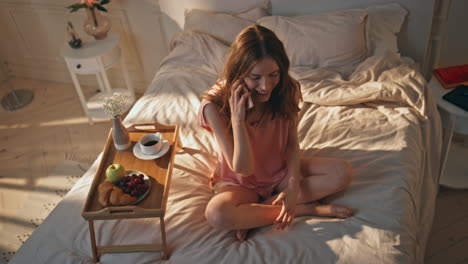 relaxed girl speaking smartphone in sunny bedroom. cheerful woman enjoying bed