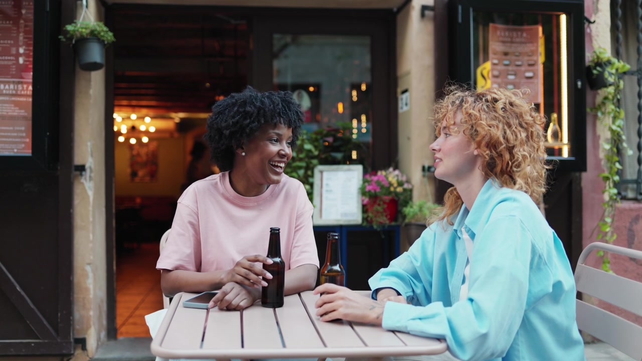 Two Diverse Friends Laughing and Socializing at an Outdoor Cafe