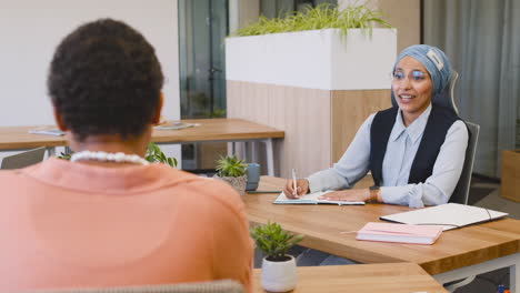 moslim zakenvrouw die aantekeningen maakt zittend op de tafel terwijl ze met haar collega's praat