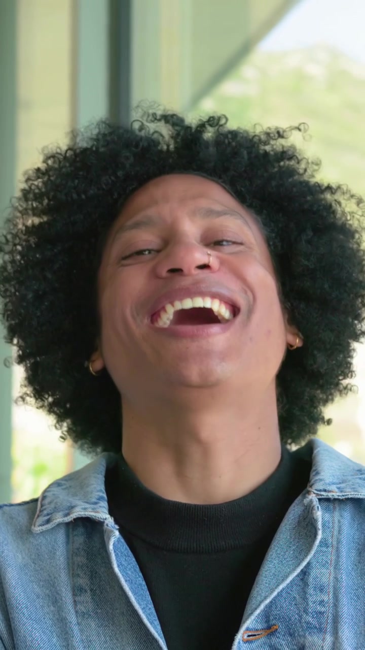 Vertical video: Hearing joke, man turning smiling laughing by window denim jacket nose ring hoops