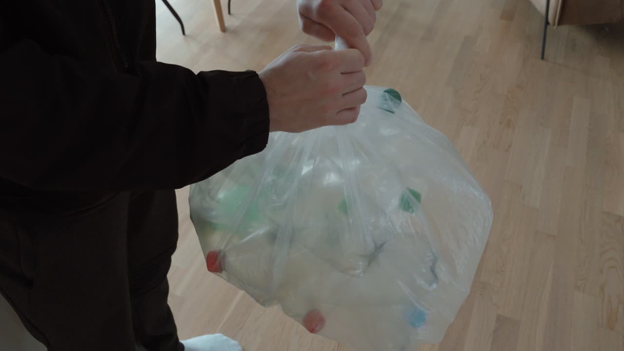 Persona che lega e solleva una borsa trasparente piena di bottiglie di plastica vuote, a simboleggiare lo smaltimento responsabile dei rifiuti, i sistemi di deposito cauzionale e un comportamento quotidiano sostenibile.
