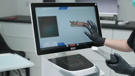 doctor scans the patient's teeth in the clinic. the dentist holds in his hand a manual 3d scanner for the jaw and mouth. dental health. creates a 3d model of teeth and gums on a medical monitor.