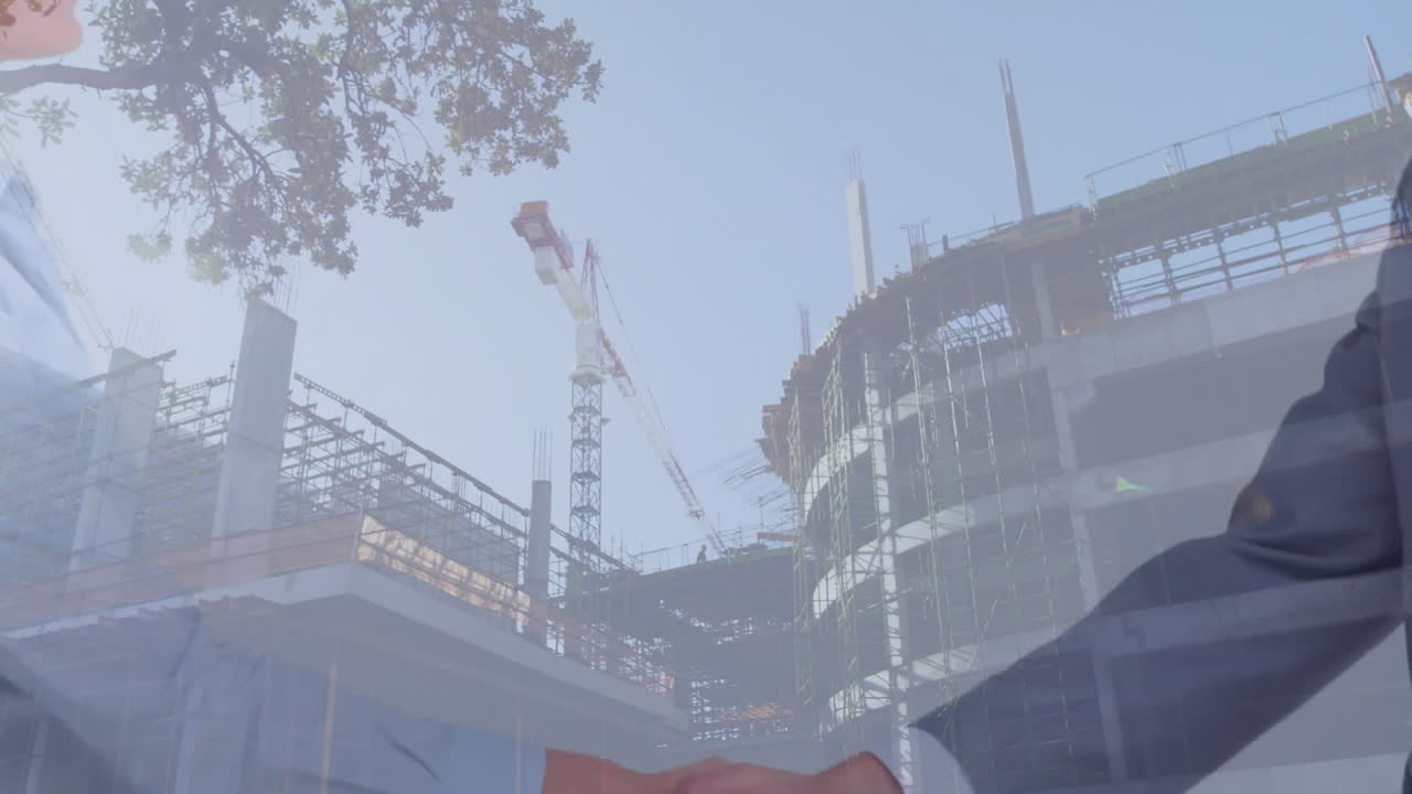 Businesspeople shaking hands at construction site with cranes and building framework