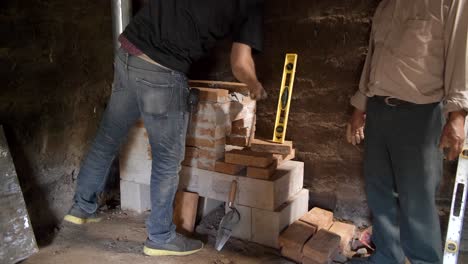 worker in small mud hut working to install brick stove mason