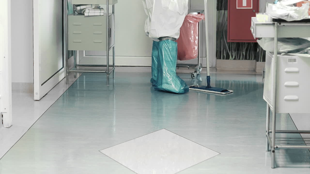 Feet Of Hospital Cleaner In Full PPE Mopping The Tiled Floor - medium shot