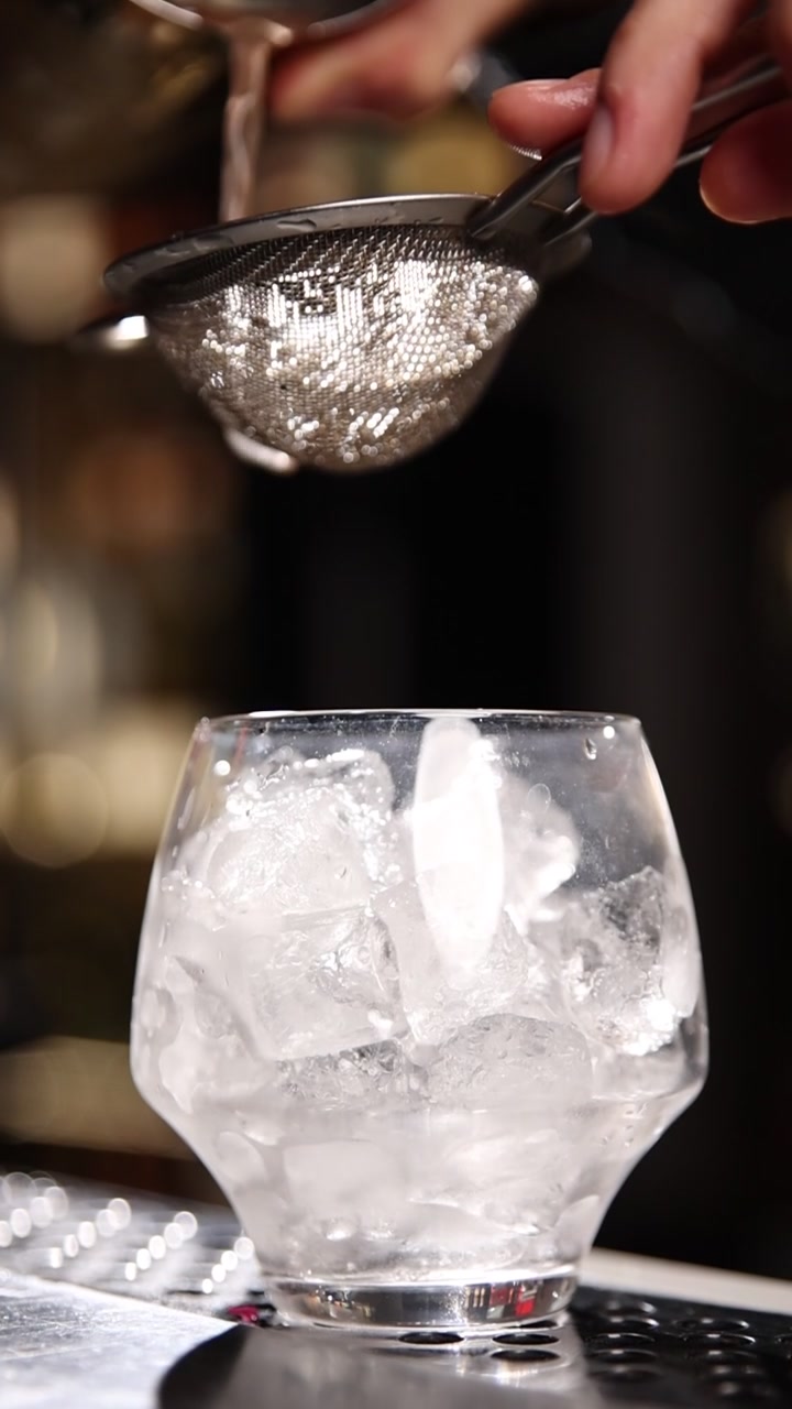 Primo piano di un barman che versa una bevanda attraverso un colino in un bicchiere ghiacciato