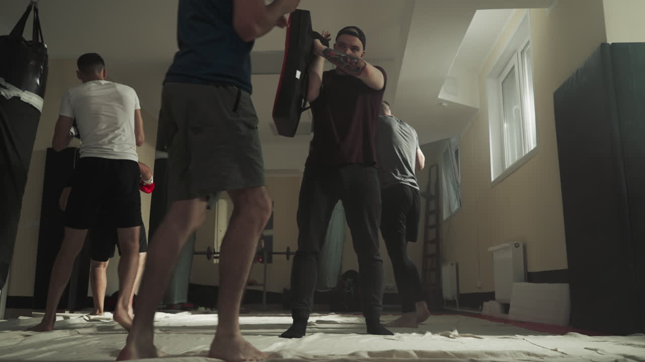 Man holds pad while partner does kicks in sports club. Kick-boxers improve fight technique together in fighting gym slow motion. Martial arts workout