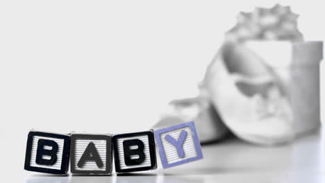 baby blocks falling over beside booties and gift box