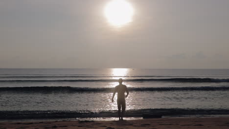 man walking towards ocean by sunrise in asia to take morning swim