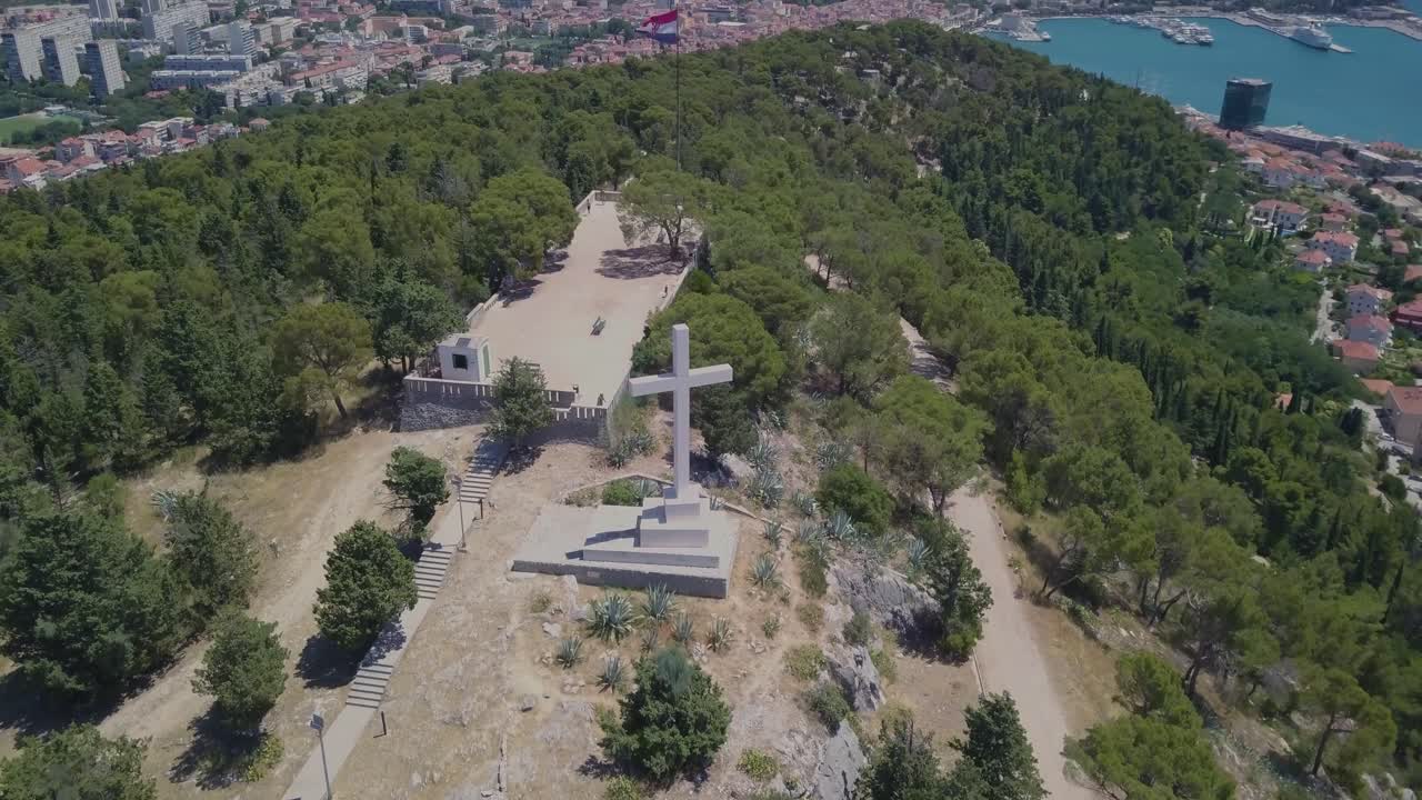 volando alrededor de la cruz de piedra blanca, manteniéndola como tema principal con el puerto y la ciudad de split al fondo