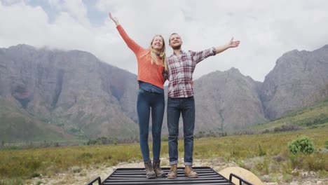 Caucasian-couple-having-a-good-time-on-a-trip-to-the-mountains,-embracing-and-raising-their-hands