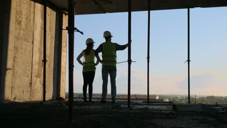 Dos-Ingenieros-Jefe-Con-Un-Dibujo-En-La-Mano-Mirando-El-Sitio-De-Construcción.-Vista-Desde-Atrás.-Ingeniero-Jefe-Con-Plano-En-Mano-Mirando-La-Construcción