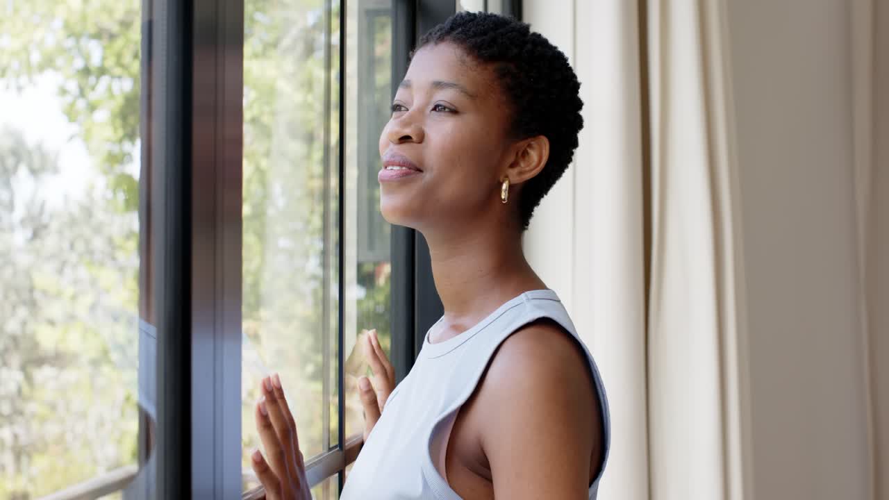 African American woman touching black frame window while sunlight drawing attention and smiling