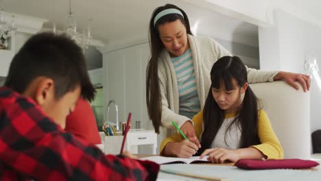 Asian-mother-in-kitchen-helping-son-and-daughter-doing-schoolwork