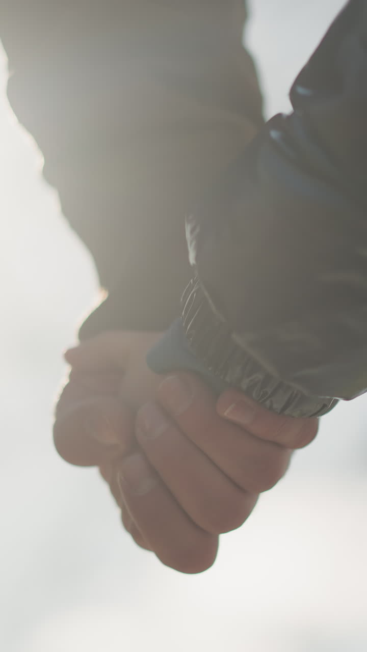 un primer plano de un adulto y un niño tomados de la mano, con la luz del sol reflejada en sus manos, el niño lleva una chaqueta negra