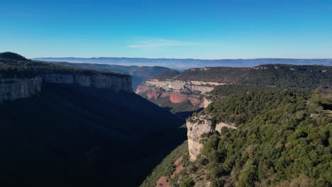 Breathtaking-aerial-view-of-the-Tavertet-cliffs-and-lush-green-forests-under-a-clear-blue-sky