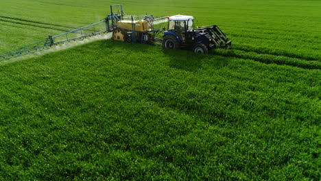 farming tractor plowing and spraying on field. drone shot of tractor spraying pesticides on green field with sprayer at spring. farm machinery spraying insecticide to the green field.