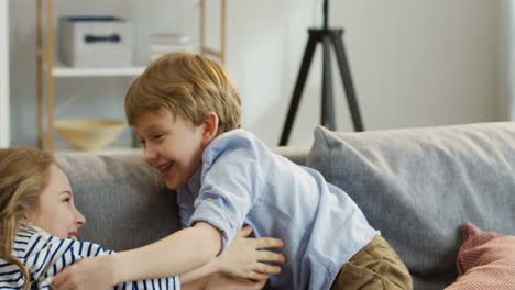 Dos-Niños-Pequeños-Y-Divertidos,-Niño-Y-Niña,-Divirtiéndose-En-El-Sofá-En-La-Acogedora-Habitación,-Haciéndose-Cosquillas-Y-Riendo