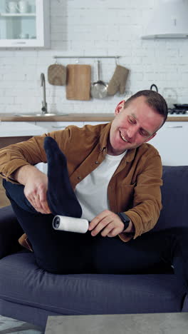 young man rests on a couch at home. funny man brushing his socks while sitting on a sofa next to laptop at home. quarantine concept. vertical video