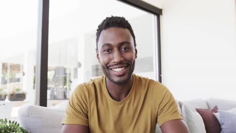 portrait of happy african american man making video call, talking in living room, in slow motion