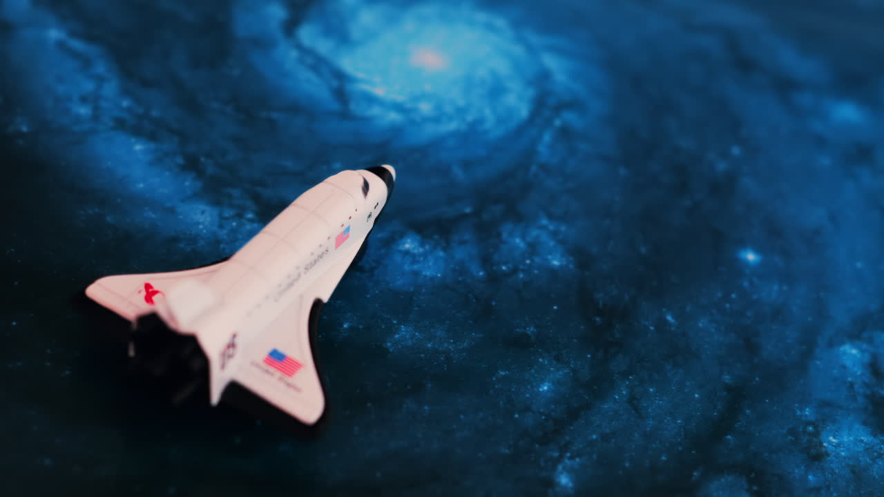 Close up of a miniature toy space shuttle placed on a blue cosmic galaxy backdrop