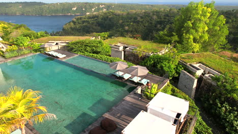 aerial tracking woman walking along swimming pool in tropical hilltop villa with panoramic overview of gamat bay at maua resort nusa penida in bali, indonesia