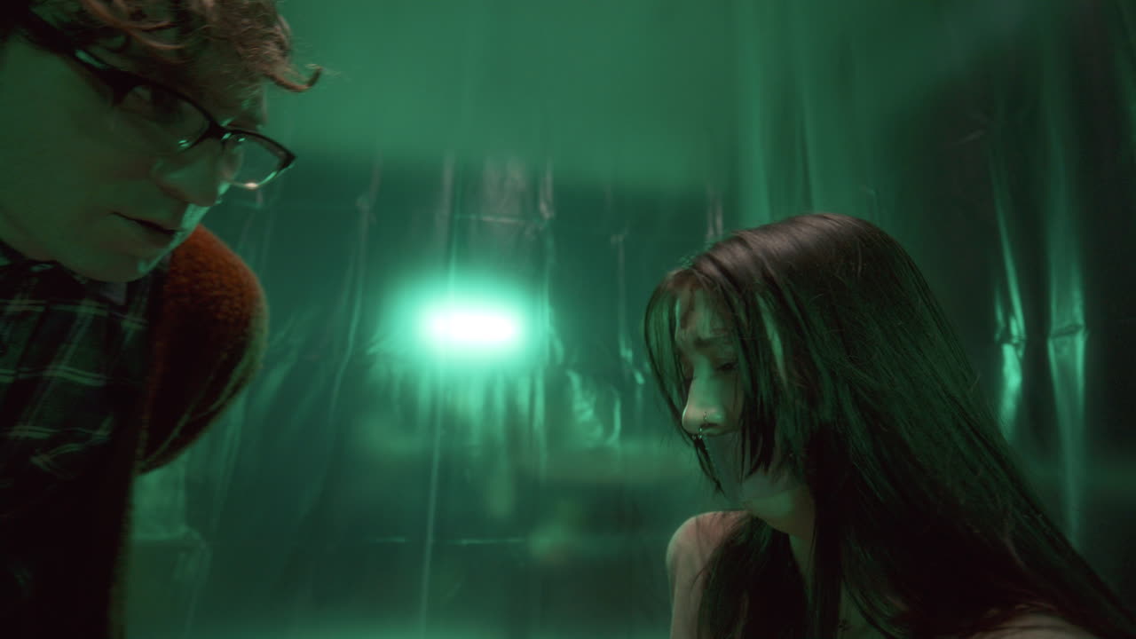 маньяк угрожает затылованным заложником, дрожащим от страха в темной комнате.