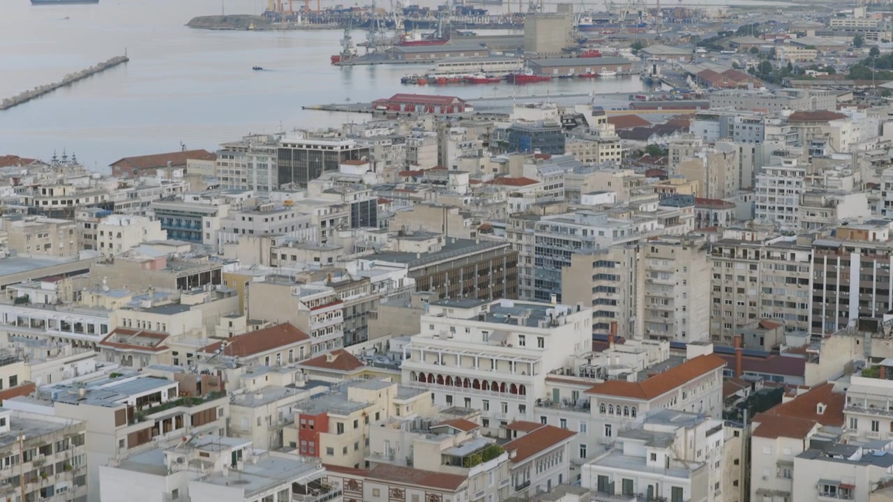 Vista aérea cercana de un alto edificio de apartamentos en Tesalónica con balcones, rodeado de densos tejados residenciales