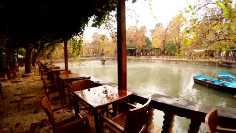 panorama empty restaurant two blue boats moor fog floats under lake ayn-zelih around green and yellow trees park urfa