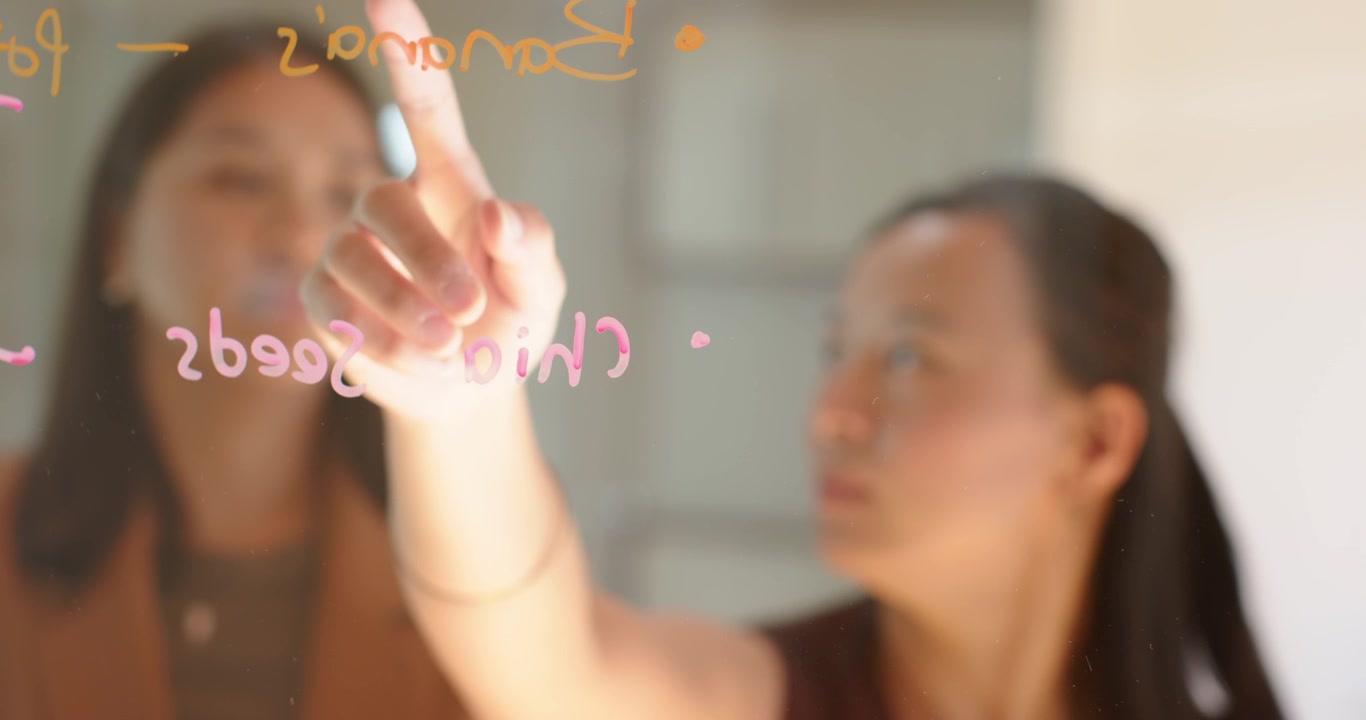 多様な女性たちがガラスパネルに表示されたチアシードを指し、マーカーでリストをなぞりながら食事の計画を立てている。