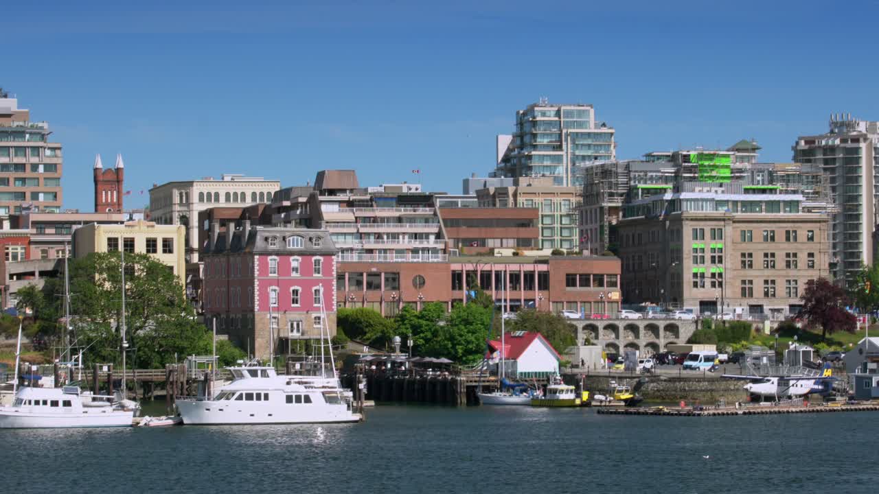 A vibrant waterfront cityscape with boats docked in the harbor, colorful buildings, and modern architecture under a clear blue sky
