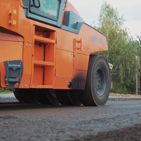 close-up of compactor machine at work on the road. heavy paver machine is pressing hot asphalt outdoors on green trees background.