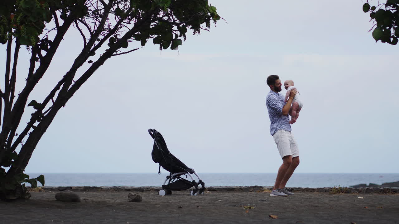 Amid the sea and beach, a portrait captures a father's tender kiss for his baby. The vacationing family radiates joy, dad holding the toddler affectionately