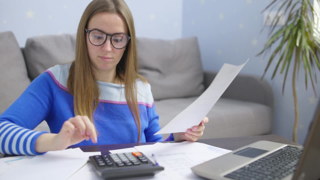 mujer usando calculadora para calcular facturas domésticas en el hogar, haciendo papeleo para pagar impuestos